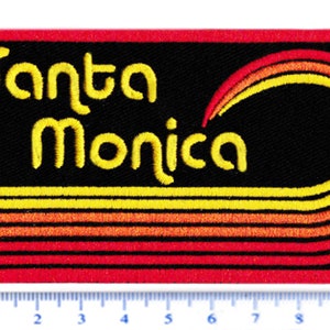 Puede incluir: Parche bordado con las palabras "Santa Monica" en amarillo. El parche tiene un fondo negro con l&iacute;neas curvas amarillas, naranjas y rojas. El borde es rojo.
