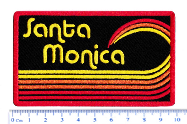 Puede incluir: Parche bordado con las palabras "Santa Monica" en amarillo. El parche tiene un fondo negro con l&iacute;neas curvas amarillas, naranjas y rojas. El borde es rojo.