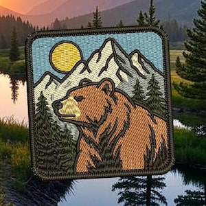 Może przedstawiać: Haftowana naszywka przedstawiająca brązowego niedźwiedzia, góry i żółte słońce na niebieskim tle. Niedźwiedź jest w profilu, z sosnami po bokach. Naszywka jest kwadratowa z ciemną obwódką, dla entuzjastów outdooru.