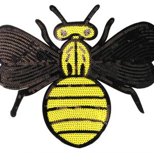 Könnte beinhalten: Eine schwarze und gelbe Bienen-Applikation mit Pailletten-Design. Die Biene hat einen gelben Körper mit schwarzen Streifen und schwarzen Flügeln.