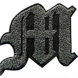 May include: A black and gray felt letter M in a gothic style.