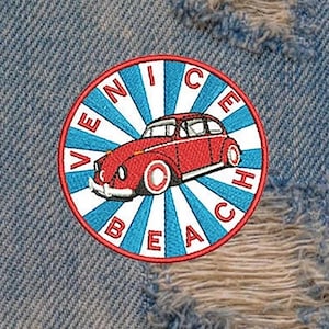 Puede incluir: Un parche circular azul y blanco con el texto "Venice Beach" en letras rojas, en el que se representa un Volkswagen Beetle rojo con techo blanco.