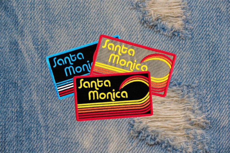 Puede incluir: Tres parches bordados con el texto "Santa Monica" en una fuente retro. Los parches presentan una forma rectangular con un dise&ntilde;o colorido de rayas y una l&iacute;nea curva, sobre un fondo de mezclilla.