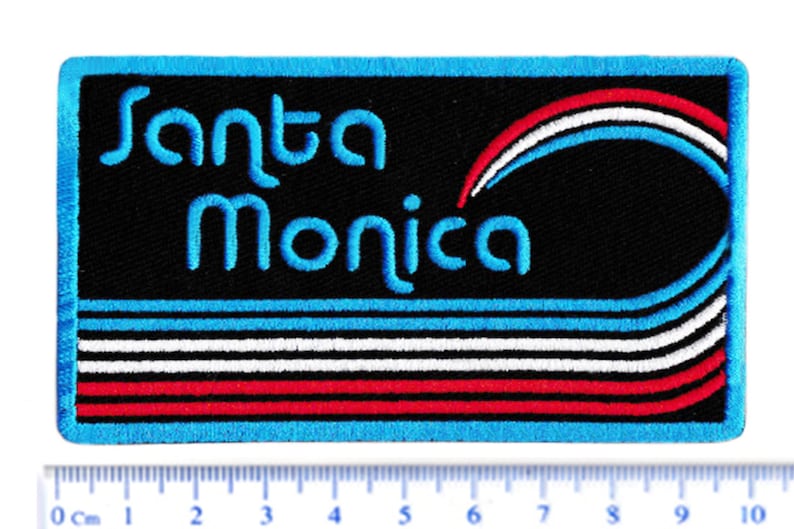 Puede incluir: Parche bordado con la frase "Santa Monica" en azul claro. El parche tiene un fondo negro con l&iacute;neas curvas azules, blancas y rojas. El borde es azul claro.