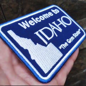 Può includere: Toppa ricamata blu e bianca con le parole "Welcome to IDAHO" e "The Gem State". La toppa presenta un contorno bianco dello stato dell'Idaho.