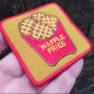 May include: Embroidered patch showing a red container of waffle fries with the text "WAFFLE FRIES" in yellow. The patch has a yellow background and a red border.