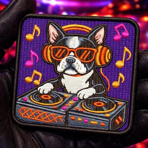 Op de afbeelding: Geborduurde patch met een Boston Terrier-hond met een oranje zonnebril en koptelefoon, die een DJ-mixer bedient. De vierkante patch heeft een paarse achtergrond met muzieknoten. De hond is zwart, wit en grijs.