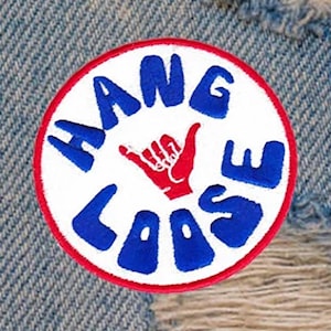 Puede incluir: Un parche circular blanco, rojo y azul con el texto "HANG LOOSE" en letras azules y una mano roja haciendo el gesto de "hang loose" en el centro.