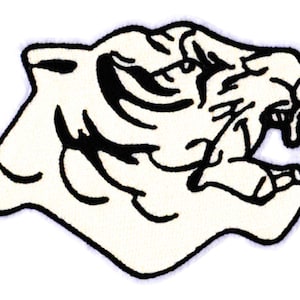 Op de afbeelding: Zwart-witte lijntekening van een tijgerkop met een open bek, waar de tanden zichtbaar zijn. De tijgerkop is naar rechts gericht.