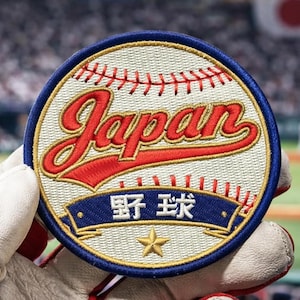 May include: Embroidered patch featuring a baseball design with the word "Japan" in red script. The patch includes Japanese characters and a gold star on a blue banner, with a white baseball background.
