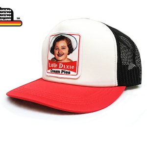 May include: White and red trucker hat with a black mesh back. The front of the hat features a patch with a woman's face and the text "Little Dixie Cream Pies".