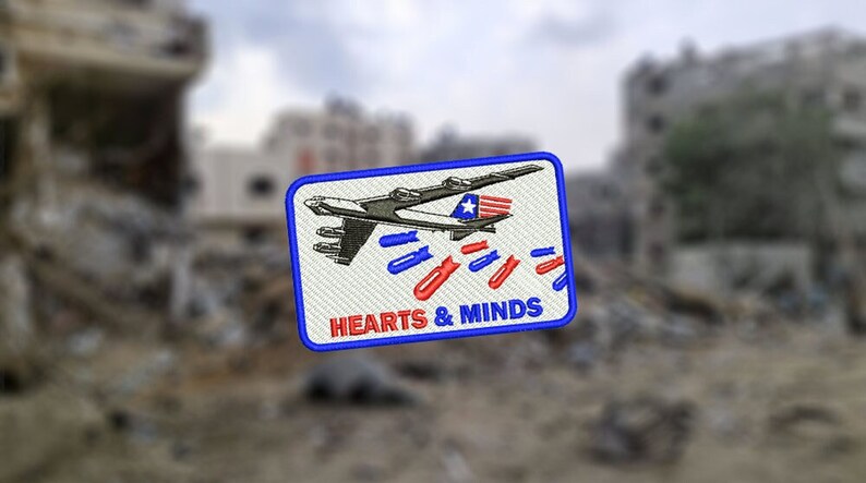 以下が含まれることがあります： 青い縁取りのある白いパッチには、赤と青のストライプの爆弾を落とす爆撃機の漫画が描かれています。飛行機の下には「HEARTS & MINDS」という文字が印刷されています。