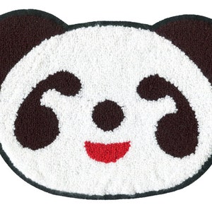 Può includere: Un tappeto di peluche bianco a forma di panda con orecchie, occhi e naso neri. Il panda ha una bocca rossa sorridente.