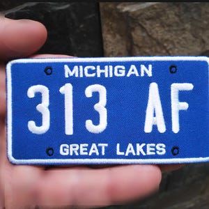 Op de afbeelding: Blauw-witte Michigan kentekenplaat patch met het nummer 313 AF en de woorden "MICHIGAN" en "GREAT LAKES".