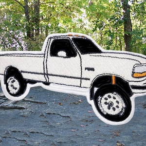 Könnte beinhalten: Weißer gestickter Aufnäher eines Pick-up-Trucks mit schwarzen Details. Der Truck hat einen schwarzen Innenraum und eine schwarze Stoßstange.