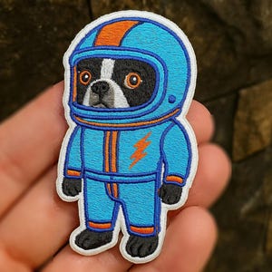 Op de afbeelding: Geborduurde patch met een Boston Terrier hond als astronaut. Het blauwe pak heeft oranje accenten en een bliksemschicht. De patch is ongeveer 7,6 cm hoog.