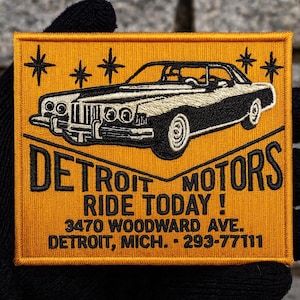 Puede incluir: Parche bordado con un diseño de coche clásico en blanco y negro sobre fondo amarillo mostaza. El parche dice "DETROIT MOTORS RIDE TODAY!" con una dirección y un número de teléfono.