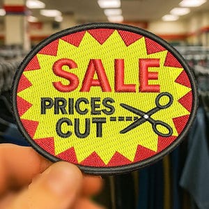 May include: Embroidered patch with a yellow starburst design and the words "SALE PRICES CUT" in red and black. A pair of scissors is featured, suggesting a price reduction. The patch is round with a black border.
