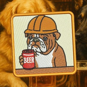 Könnte beinhalten: Gestickter Aufnäher mit einer Bulldogge, die einen Bauhelm trägt und eine Bierdose hält. Auf der Dose steht das Wort "BEER". Der quadratische Aufnäher hat einen goldenen Rand, vor einem Hintergrund von Hunden.