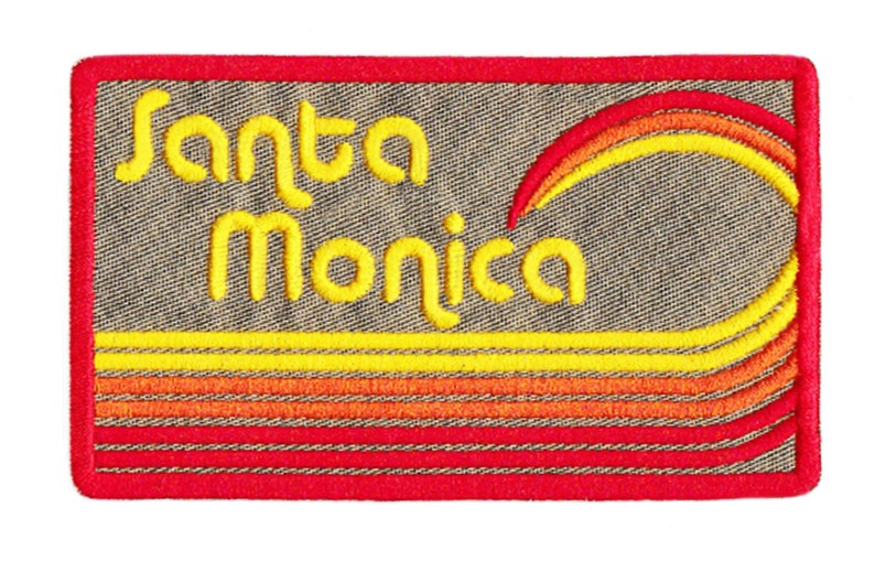 Puede incluir: Parche bordado con las palabras "Santa Monica" en escritura amarilla. El parche tiene un borde rojo y presenta un dise&ntilde;o de puesta de sol estilizado en amarillo, naranja y rojo. El fondo es una tela gris texturizada.