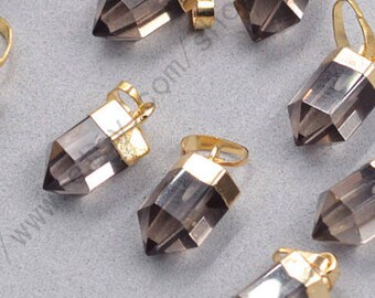 Puede incluir: Un conjunto de colgantes de cristal de cuarzo ahumado con tapas y bucles de metal dorado. Los colgantes son facetados y tienen forma puntiaguda. Fondo gris claro. Ideales para la creación de joyas.
