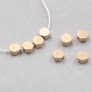May include: A gold necklace with a string of hexagonal beads. The necklace is on a grey surface.