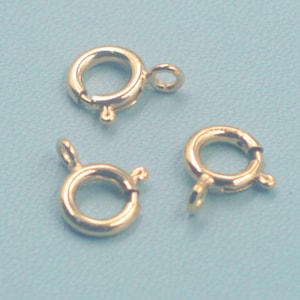 May include: Three gold-colored spring ring clasps on a light blue background. The clasps are circular with a small loop and a spring mechanism for secure closure. Ideal for jewelry making.