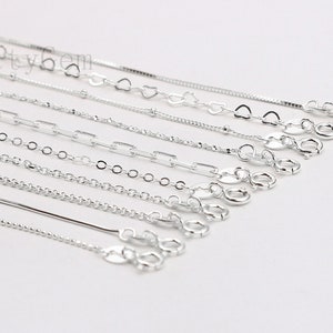 May include: A collection of silver chains in various styles and lengths. The chains are laid out in a row, with the clasps at the bottom of the image.
