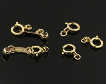 Pode incluir: Cinco fechos de metal dourado para a fabricação de joias. Dois fechos têm uma pequena bola em cada extremidade, e três fechos têm um único anel em uma extremidade.
