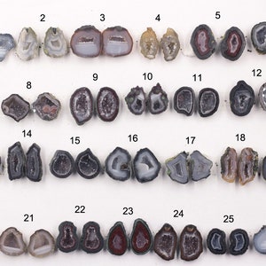 Puede incluir: Una colección de 26 mitades de geodas de ágata, cada una con un patrón único de cristales y colores. Las geodas están dispuestas en filas de cuatro, con una moneda de 1 euro para la escala.