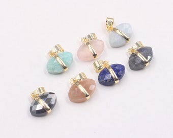 May include: Seven gemstone pendants in various colors, including blue, pink, and gray. Each pendant features a faceted oval gemstone with a gold-colored metal band and bail. The pendants are displayed on a white surface.