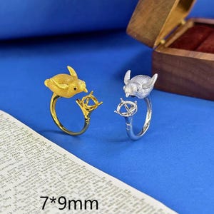 May include: Two rings featuring a bird-shaped design, one in a gold tone and one in a silver tone. Each ring has a prong setting for a gemstone, with the text 7*9mm printed on the surface below the rings, indicating the stone size.