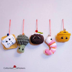 May include: Five crocheted ornaments hanging from red strings. The ornaments are a slice of bread, a broccoli, a Christmas pudding, a shrimp, and a yellow bowl. Each ornament has a cute face.