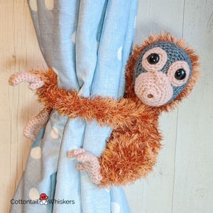 May include: A crocheted orangutan holding a blue and white polka dot curtain. The orangutan is brown with a gray face and large black eyes. The orangutan is holding the curtain with its arms and legs.