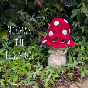 May include: A crocheted toadstool figure with a red cap featuring white spots, a sad facial expression with large black eyes, and a beige stem. The text "NORMAN THE TOADSTOOL" is printed on the left, and "Cottontail Whiskers" is at the bottom.