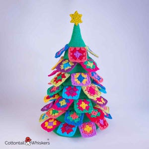May include: A handmade crochet Christmas tree with colorful square ornaments. The tree is green with a yellow star on top. The ornaments are various colors, including pink, blue, yellow, and purple. The base of the tree is also green.