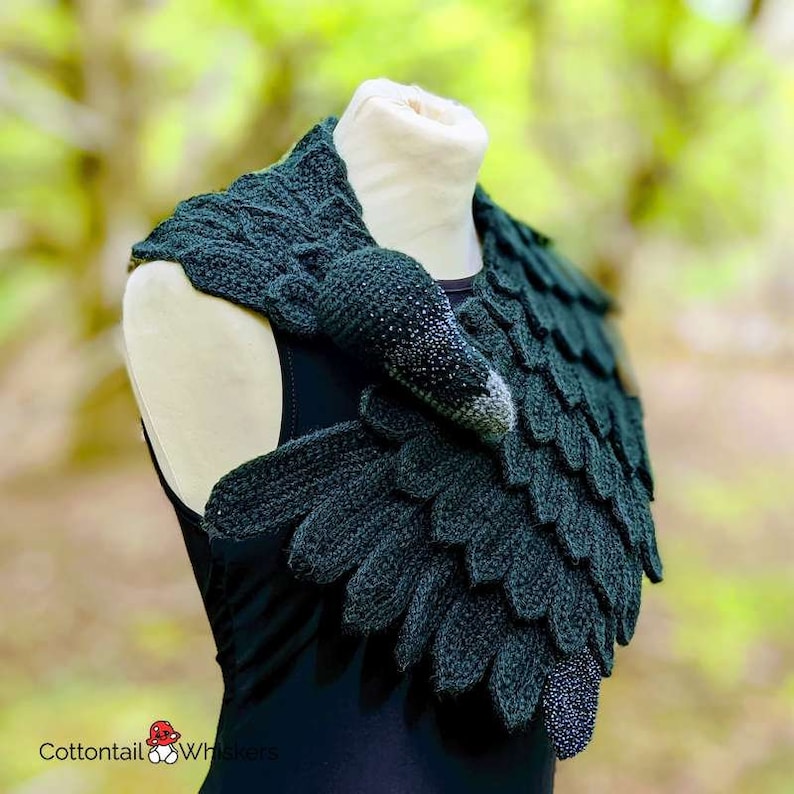 May include: A dark green crocheted scarf shaped like a bird with a long neck and beak. The scarf is worn around the neck of a mannequin.