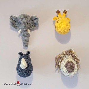 Puede incluir: Cuatro decoraciones de pared de cabeza de animal de crochet. Los animales son un elefante, una jirafa, un rinoceronte y un le&oacute;n. El elefante es gris, la jirafa es amarilla, el rinoceronte es azul y el le&oacute;n es marr&oacute;n. Los animales est&aacute;n todos mirando hacia adelante y tienen una apariencia 3D.