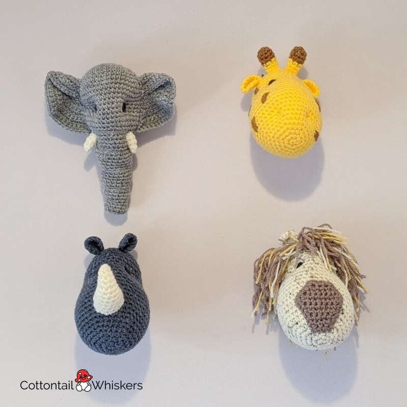 Puede incluir: Cuatro decoraciones de pared de cabeza de animal de crochet. Los animales son un elefante, una jirafa, un rinoceronte y un le&oacute;n. El elefante es gris, la jirafa es amarilla, el rinoceronte es azul y el le&oacute;n es marr&oacute;n. Los animales est&aacute;n todos mirando hacia adelante y tienen una apariencia 3D.