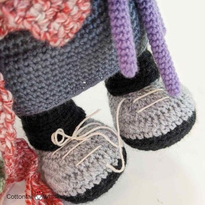 Pode incluir: Close-up dos p&eacute;s de uma boneca de croch&ecirc; usando sapatos cinzentos com solas pretas. Os sapatos t&ecirc;m detalhes de costura branca.