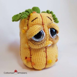 May include: A crocheted pumpkin plush toy with a sad expression, green leaves on top, and brown stitching. The pumpkin is yellow with orange and yellow accents.