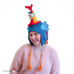 Puede incluir: Un gorro de ganchillo hecho a mano con forma de gallo. El gorro presenta una base azul con una cresta roja, una cabeza amarilla y patas colgantes naranjas. El gorro está diseñado para ser usado y es un accesorio divertido y único.