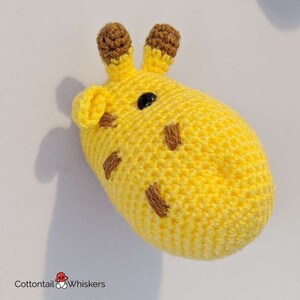 Puede incluir: Una cabeza de jirafa de crochet con orejas marrones y un ojo negro. La jirafa es amarilla con manchas marrones.