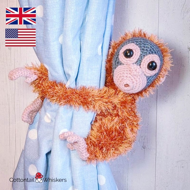 May include: A crocheted monkey curtain tieback in orange and gray with a light blue background. The monkey is holding the curtain tieback with its arms.