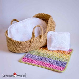 May include: A handmade crochet baby set. It includes a tan bassinet with handles, a white pillow, a small white square pillow, and a rainbow-striped blanket. The set is designed for a baby.