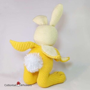 May include: A crocheted yellow bunny with white ears and a fluffy white tail. The bunny is sitting on its hind legs with its front paws outstretched.