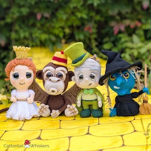 May include: Four crocheted characters from the Wizard of Oz: a white-dressed Dorothy, a brown monkey with wings, a green-clothed Tin Man, and a black-dressed Wicked Witch of the West. The characters are standing on a yellow brick road.
