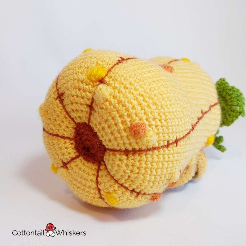 May include: A crocheted yellow cactus with brown and orange stitching and yellow and orange accents. The cactus is lying on its side.