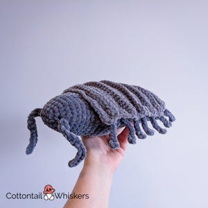 May include: Gray crocheted plush toy shaped like a pill bug. The toy has segmented body parts and small legs.