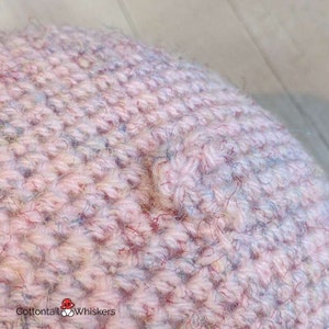 Op de afbeelding: Close-up van een roze gebreide muts met een textuur. De muts is gemaakt van een veelkleurig garen in roze, blauwe en witte tinten.